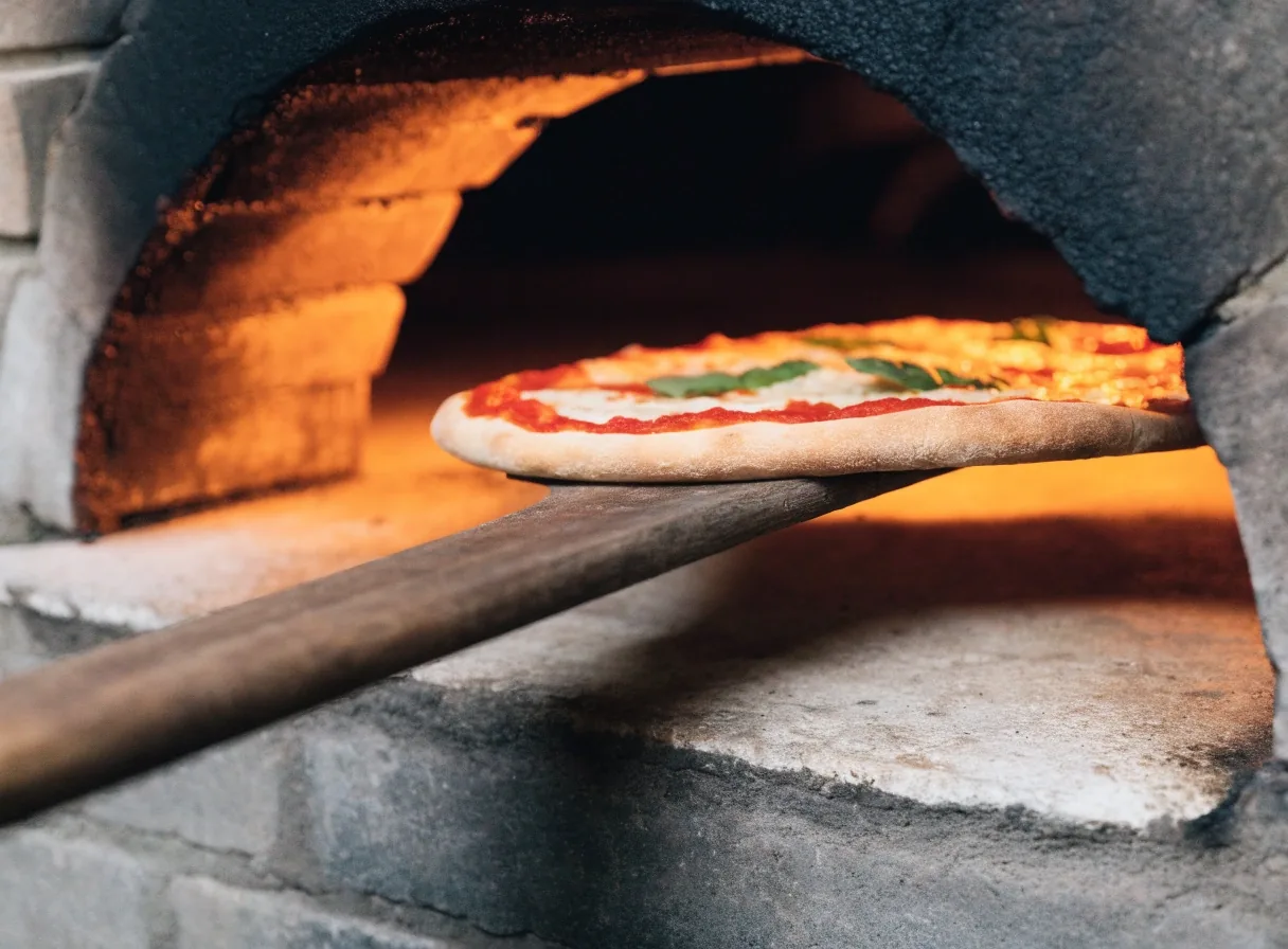 Pizza sliding into a hot oven on a wooden peel